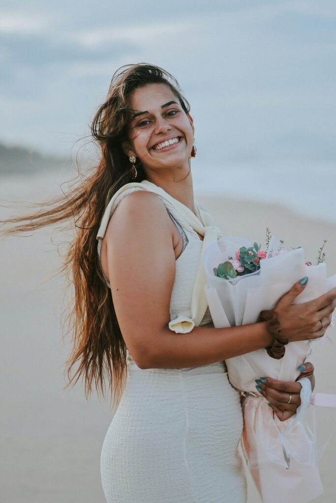 A smiling woman holding a bouquet on the beach